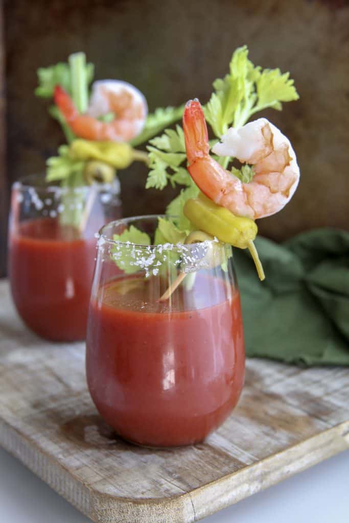 two keto bloody marys in glasses garnished with shrimp and pepperoncini 