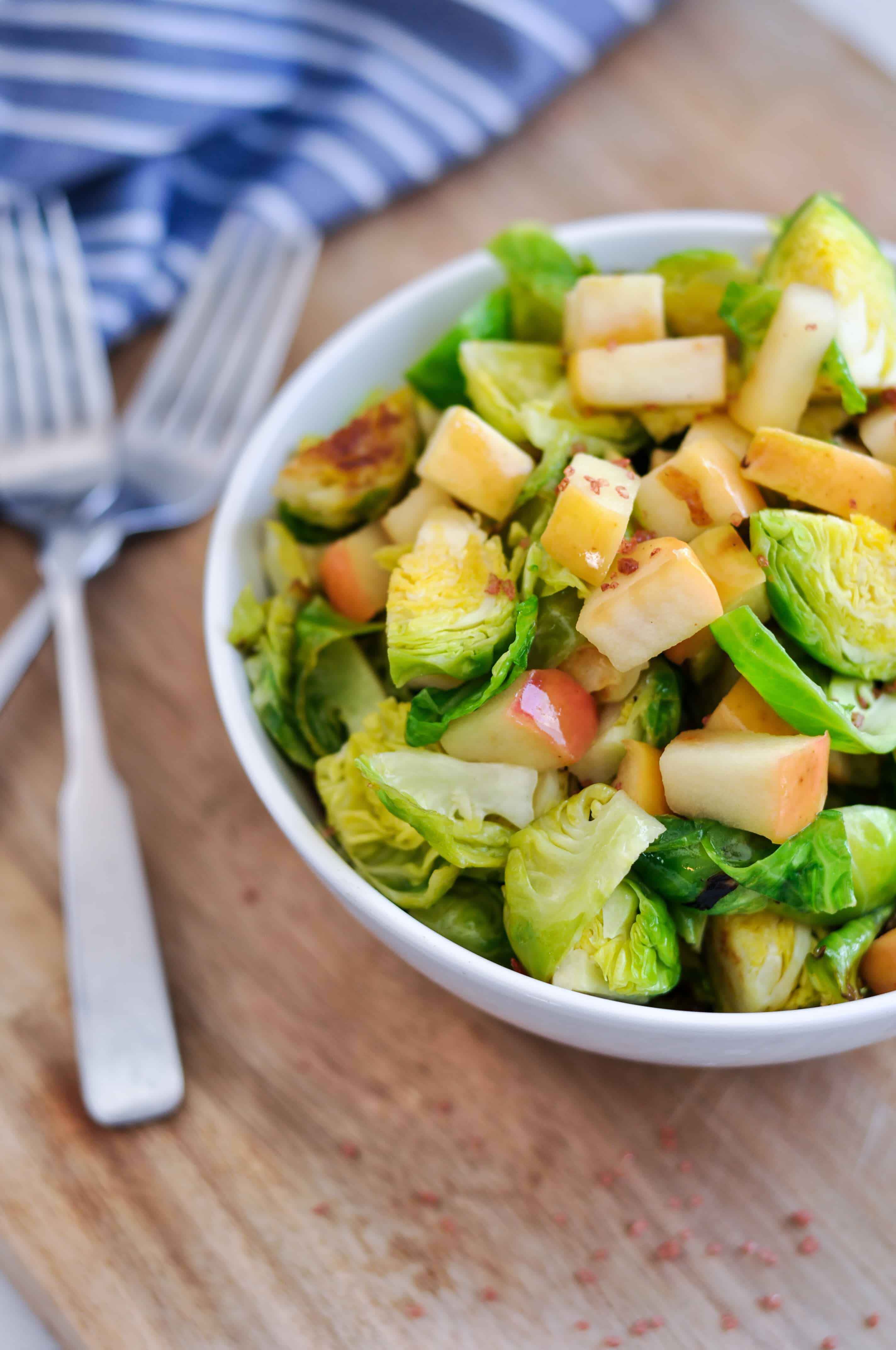 brussels sprouts and apples in a bowl next to forks