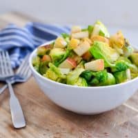 brussels sprouts salad with apples in a bowl next to forks