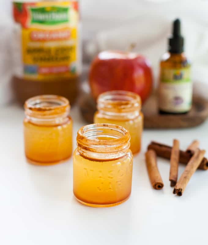 3 apple cider vinegar shots on a table with cinnamon and apple