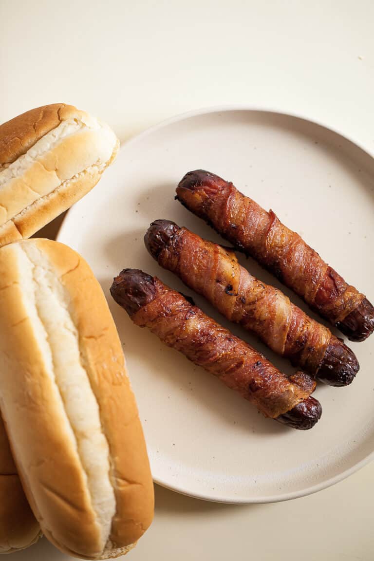 bacon wrapped hot dogs on a plate with buns