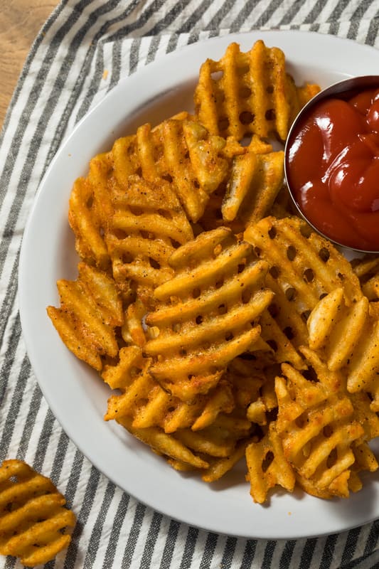 cooked waffle fries on a plate with ketchup