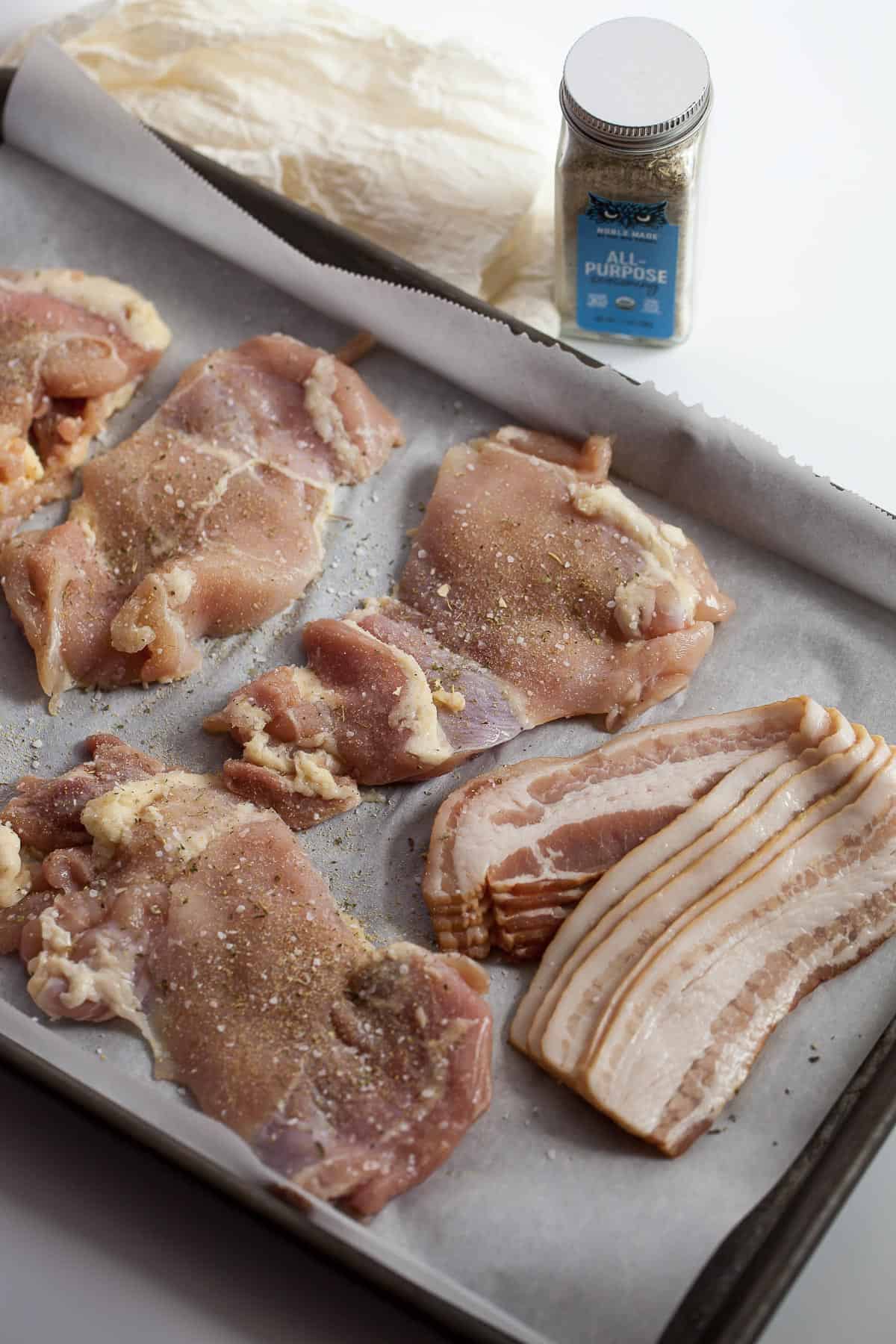 seasoned chicken thighs with bacon on a sheet pan