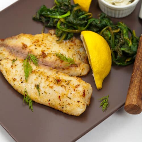 tilapia on a plate with herbs and lemons
