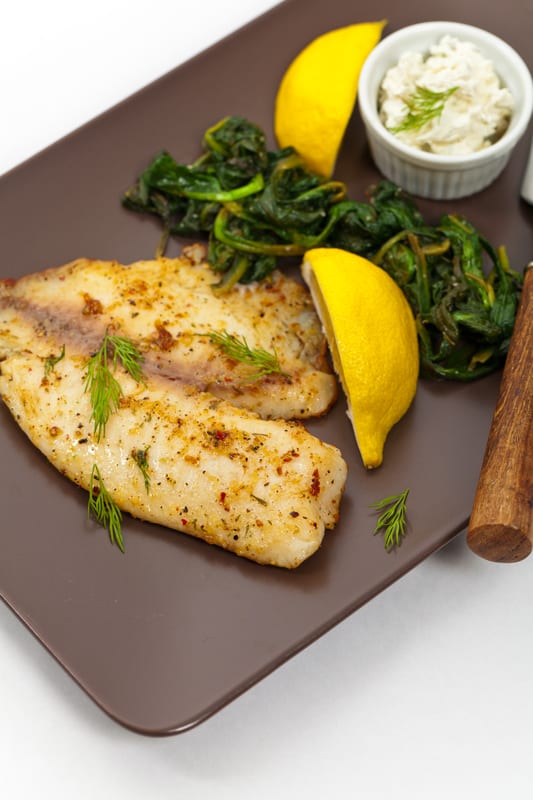 tilapia on a plate with herbs and lemons