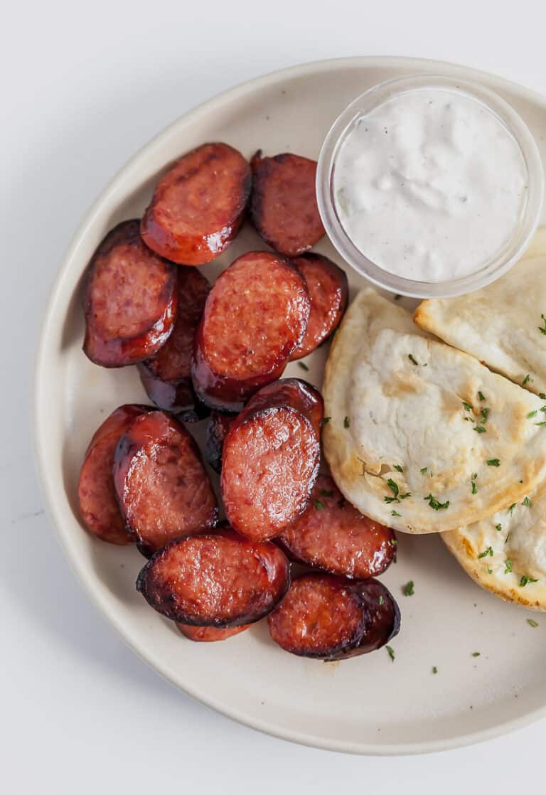 sliced smoked sausage on a plate with pierogies and sour cream